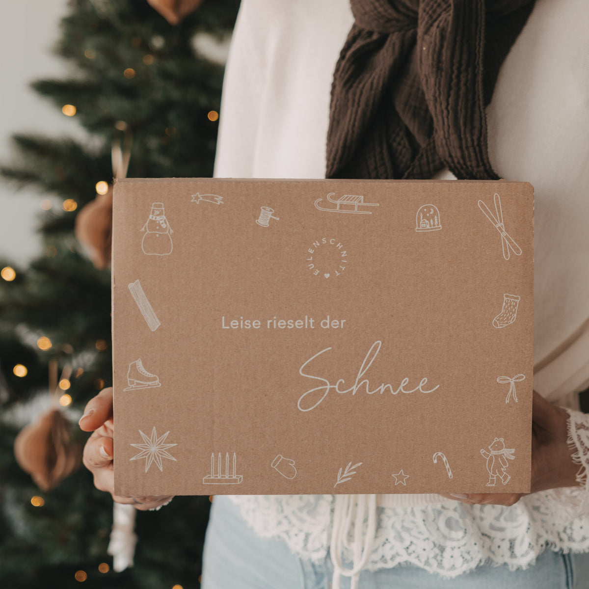 Limitierte Winter-Überraschungsbox 2026 von Eulenschnitt mit winterlichen Illustrationen und Schriftzug „Leise rieselt der Schnee“, vor einem geschmückten Weihnachtsbaum gehalten.
