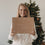 Lächelnde Frau hält die limitierte Winter-Überraschungsbox 2026 von Eulenschnitt mit liebevollen Wintermotiven vor einem beleuchteten Weihnachtsbaum.