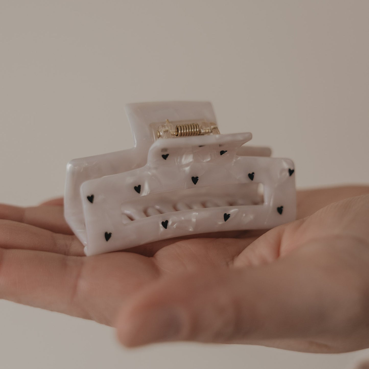 Große eckige Haarspange in Perlmutt-Optik mit schwarzen Herzen in der Hand präsentiert