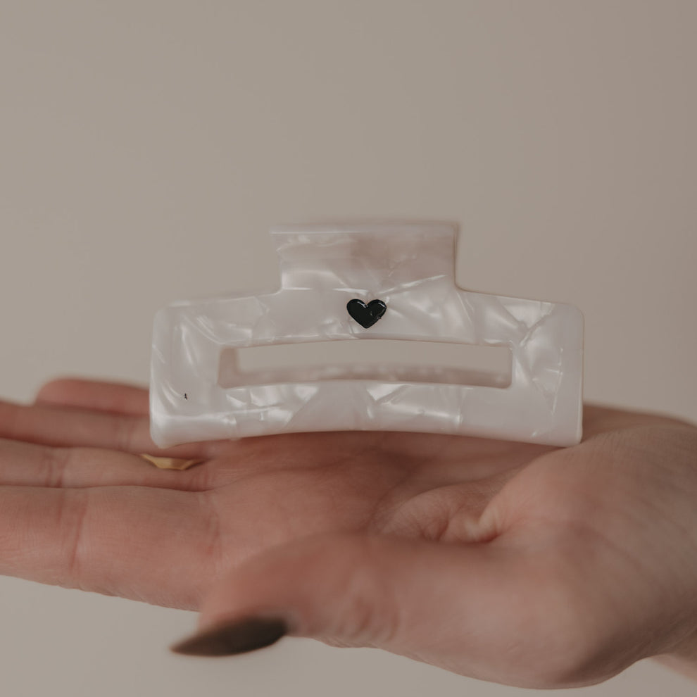 Große eckige Haarspange in Perlmutt-Optik mit schwarzem Herz in der Hand präsentiert