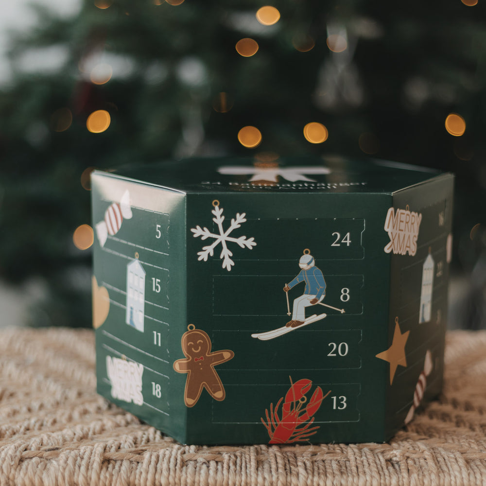 Grüner Eulenschnitt Adventskalender mit 24 Baumanhängern aus Metall vor einem Weihnachtsbaum