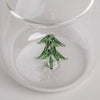 Trinkglas mit grüner Tannenfigur aus Glas im Boden, rund und transparent