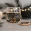 Nahaufnahme Glas mit goldfarbenem Stern im Boden, weihnachtliche Atmosphäre mit Lichterkette und Orangenscheiben