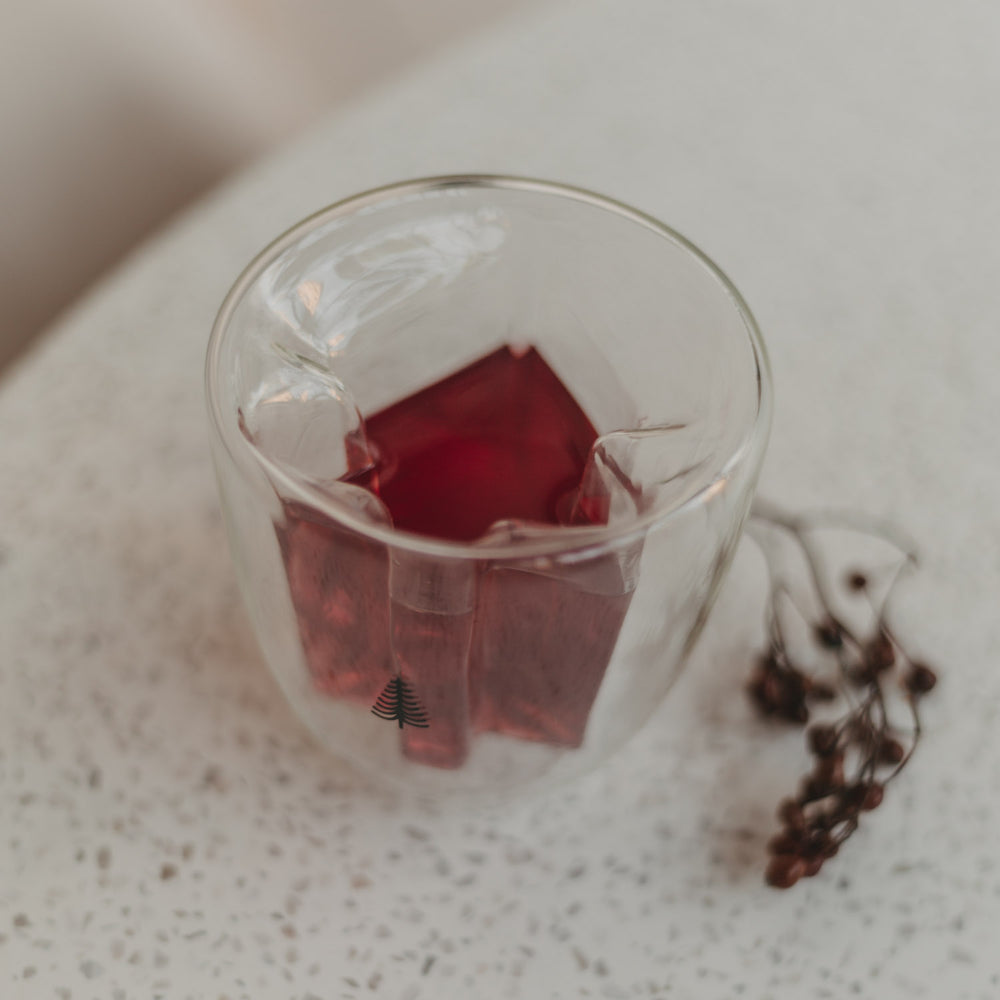 Doppelwandiges Tannenglas mit rotem Getränk, Seitenansicht zeigt dreidimensionale Baumform.