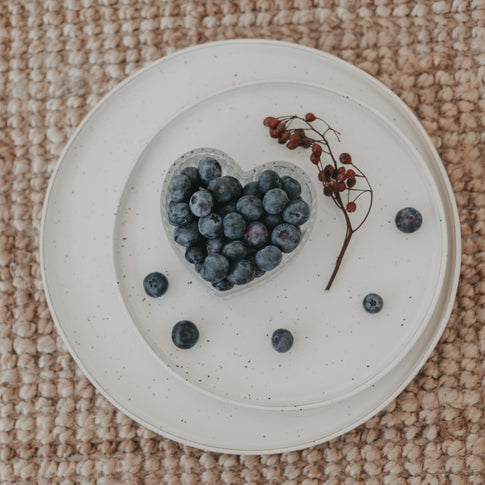 Herzschale aus Glas mit Blaubeeren, angerichtet auf weißem Teller, ideal für Frühstück oder Snacks.
