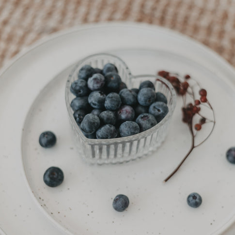 Detailaufnahme der Herzschale gefüllt mit Blaubeeren und dekorativem Zweig.