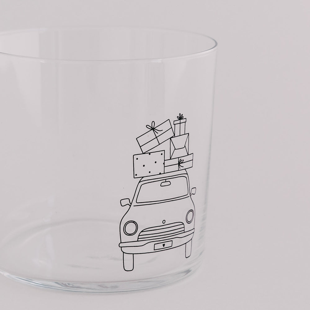 Nahaufnahme des Trinkglases mit Auto und Geschenkstapel – feines Weihnachtsmotiv.