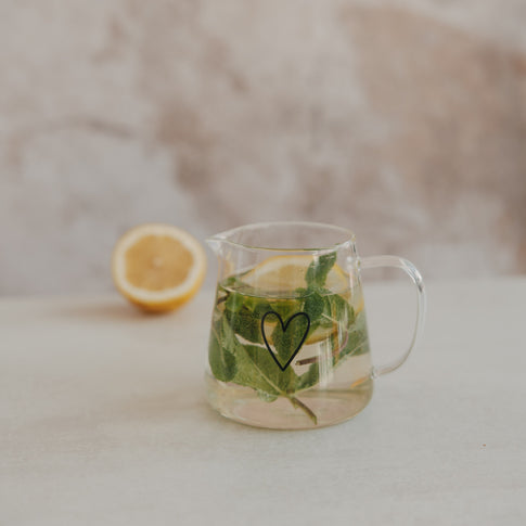 Glas Teekanne mit Herzmotiv, gefüllt mit Wasser, Minze und Zitrone, stilvoll für Tee und Infused Water