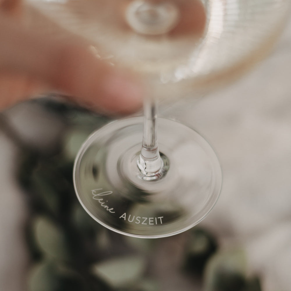 Fokus auf Gravur „kleine Auszeit“ am Glasboden – stilvolles Detail beim Hochheben des Glases.