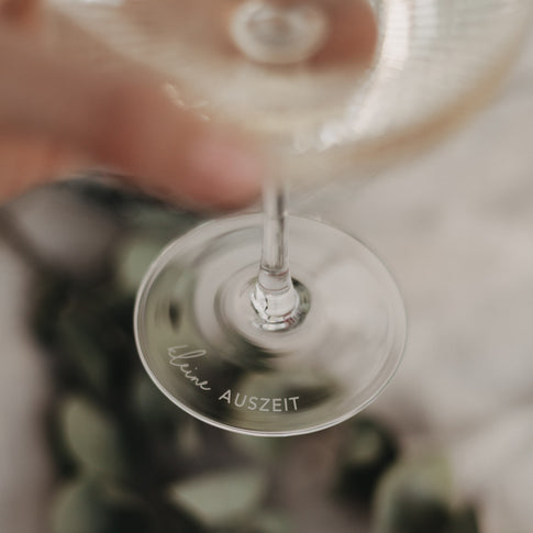 Fokus auf Gravur „kleine Auszeit“ am Glasboden – stilvolles Detail beim Hochheben des Glases.