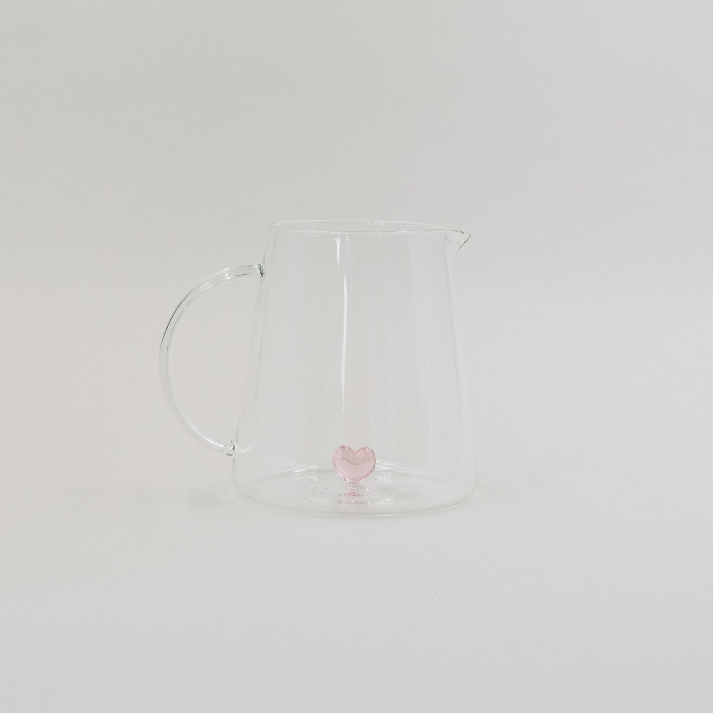 Karaffe aus Glas mit rosa Herzfigur im Inneren, minimalistisch vor weißem Hintergrund inszeniert.