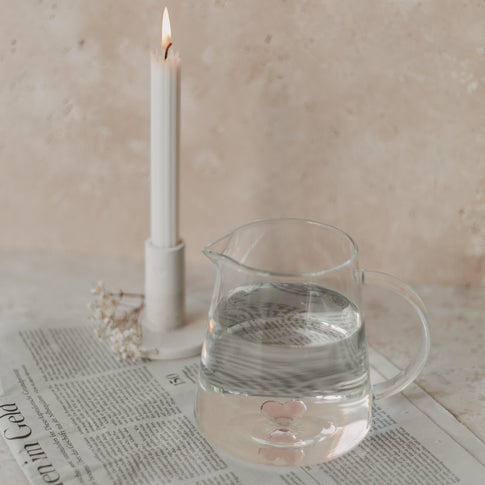Glaskaraffe mit rosa Herz neben Kerze auf Zeitung – stimmungsvolle, liebevolle Tischdeko.