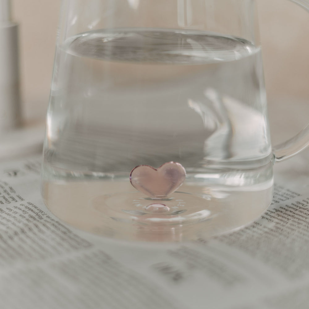 Seitlicher Blick durch klares Wasser auf die rosa Herzfigur im Inneren der Karaffe.