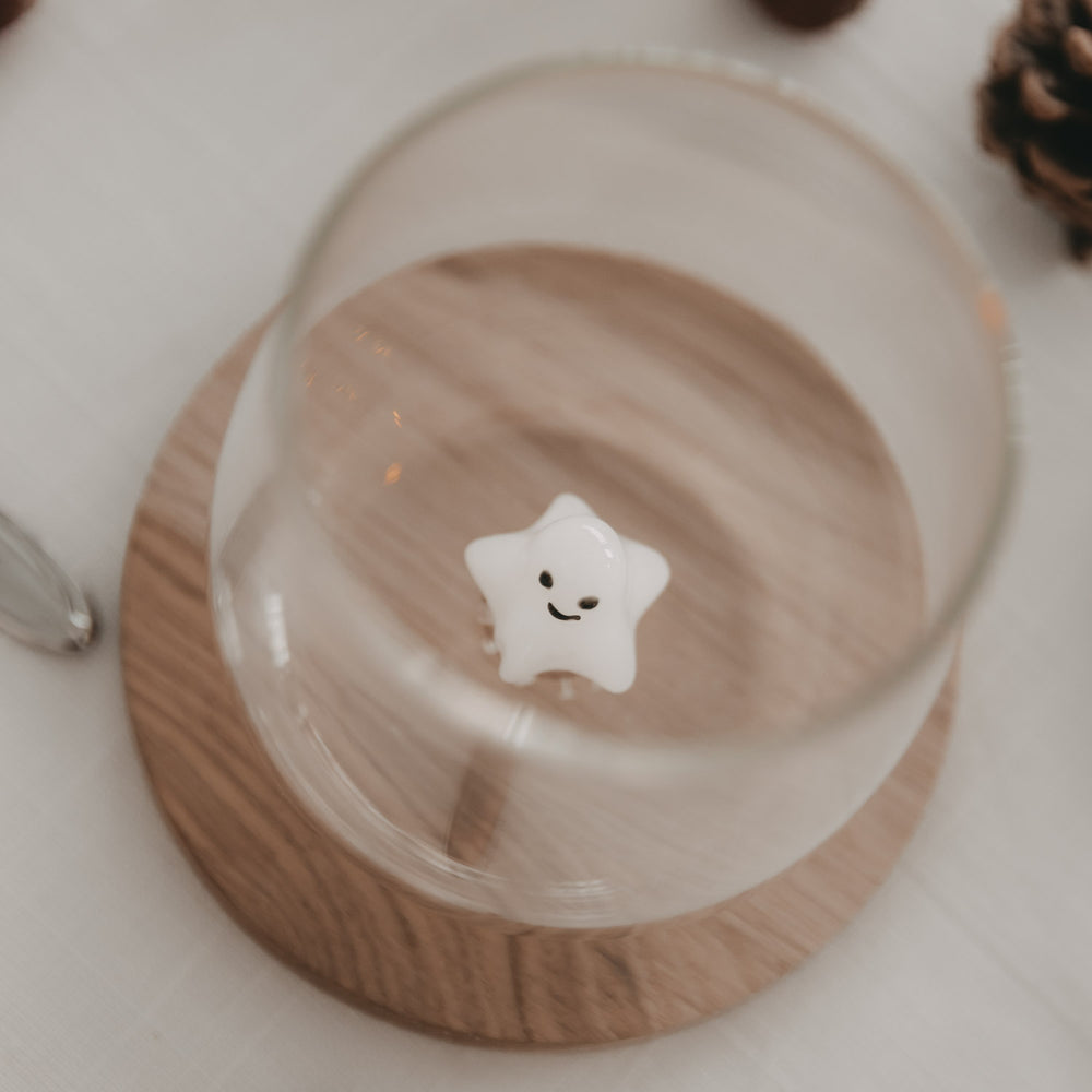 Oberansicht auf Trinkglas mit 3D-Sternfigur aus Glas, stilvoll auf Holzuntersetzer mit Deko platziert