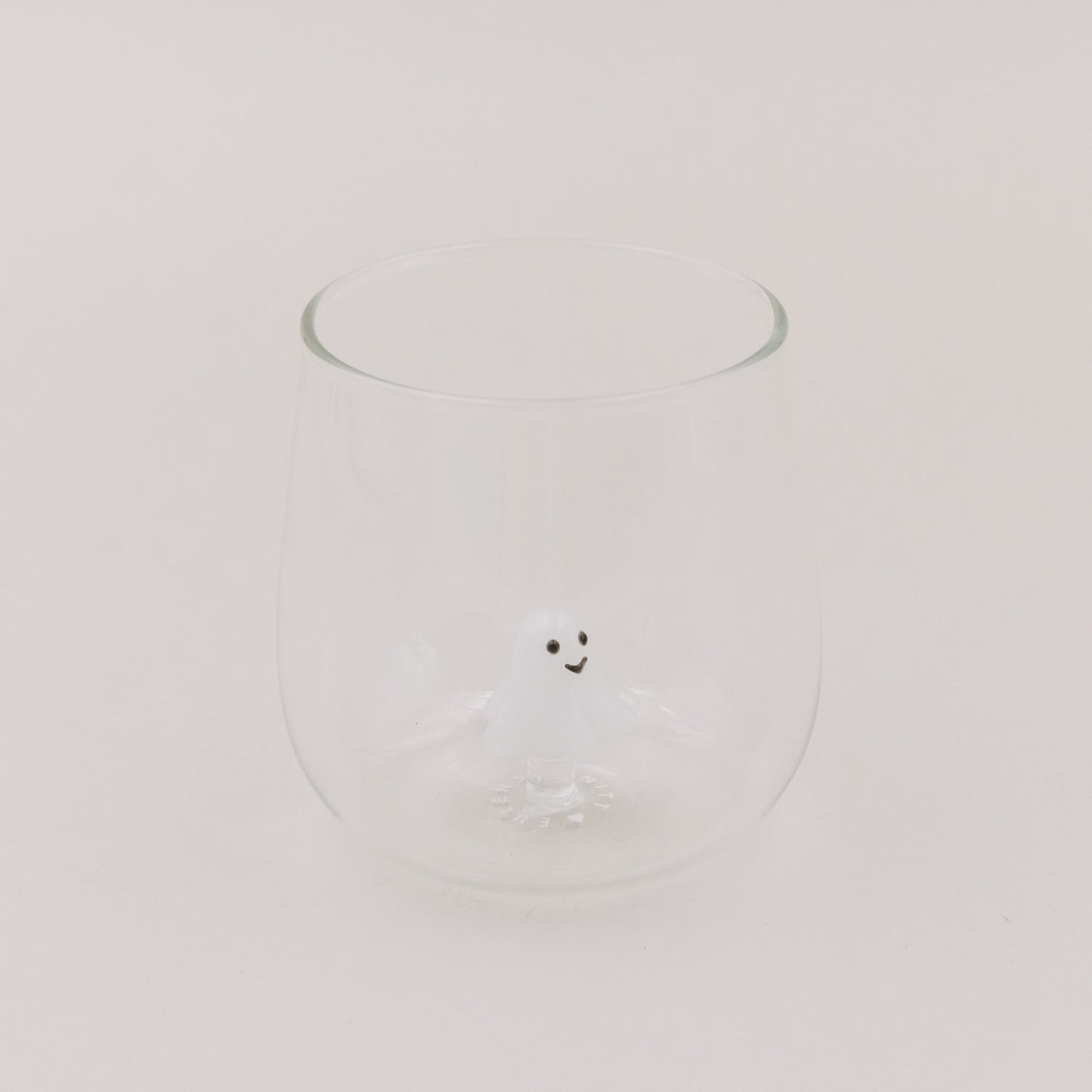 Glas mit kleiner weißer Geistfigur als 3D-Detail am Glasboden, hell und minimalistisch inszeniert