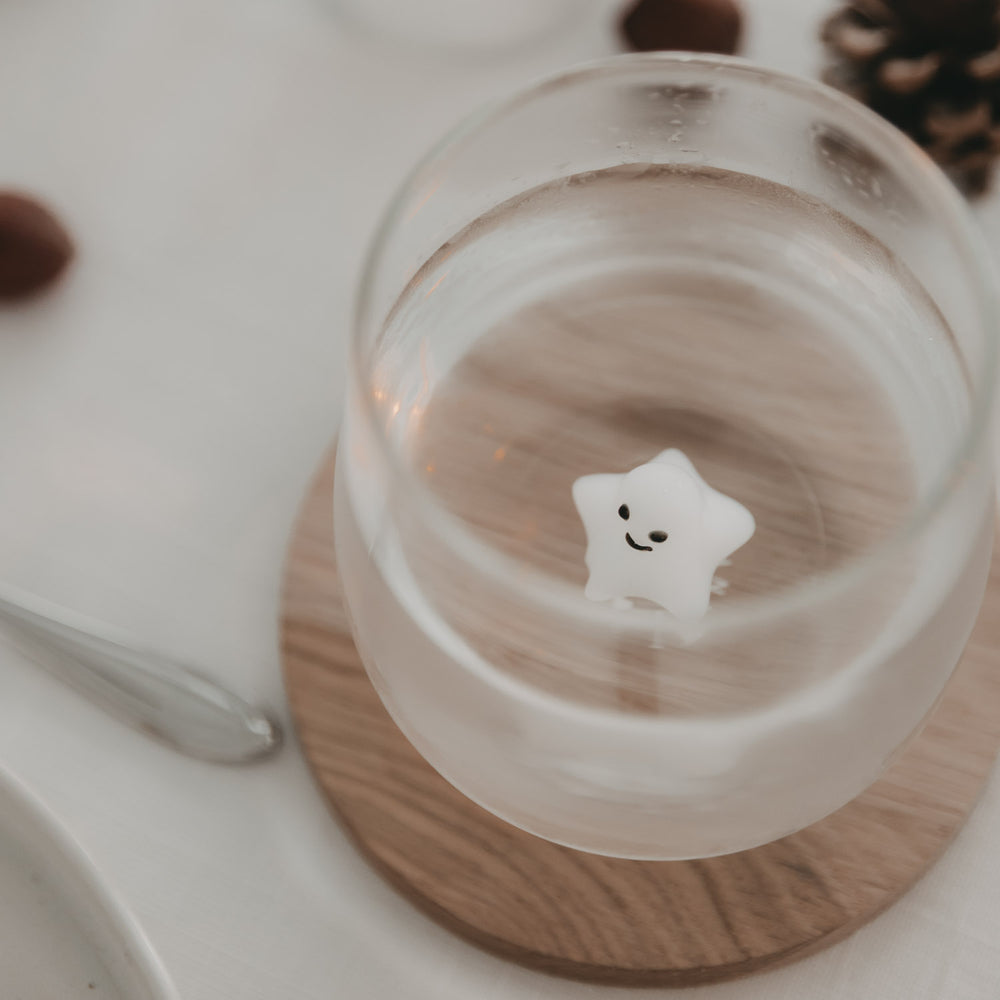 Von oben fotografiertes Trinkglas mit 3D-Sternfigur auf einem runden Holzuntersetzer