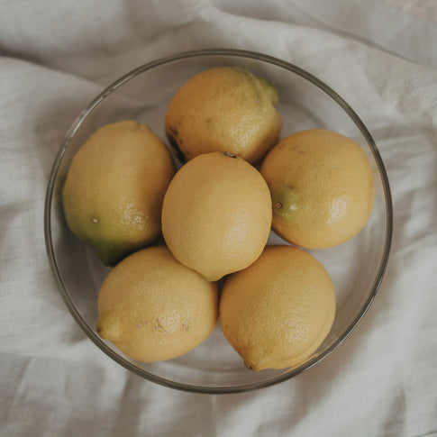 Obere Ansicht einer Glas-Schale mit Zitronen, dekorativ arrangiert auf einem hellen Stoff.