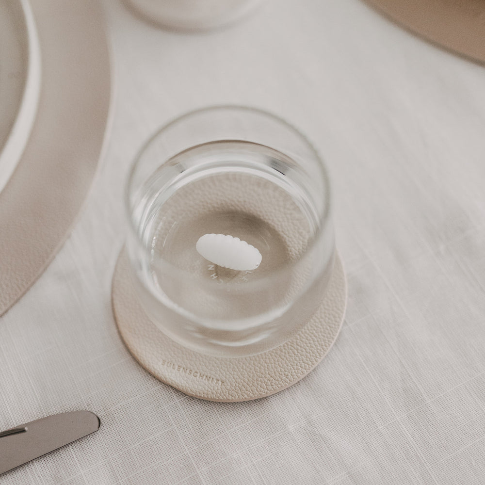 Draufsicht auf Trinkglas mit Muschelmotiv am Boden auf strukturiertem Untersetzer