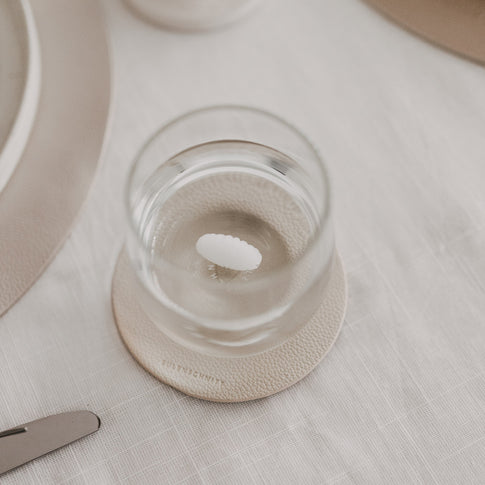 Draufsicht auf Trinkglas mit Muschelmotiv am Boden auf strukturiertem Untersetzer