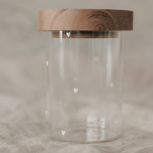 Kleines Vorratsglas mit weißen Herzmotiven und Holzdeckel auf hellem Stoff