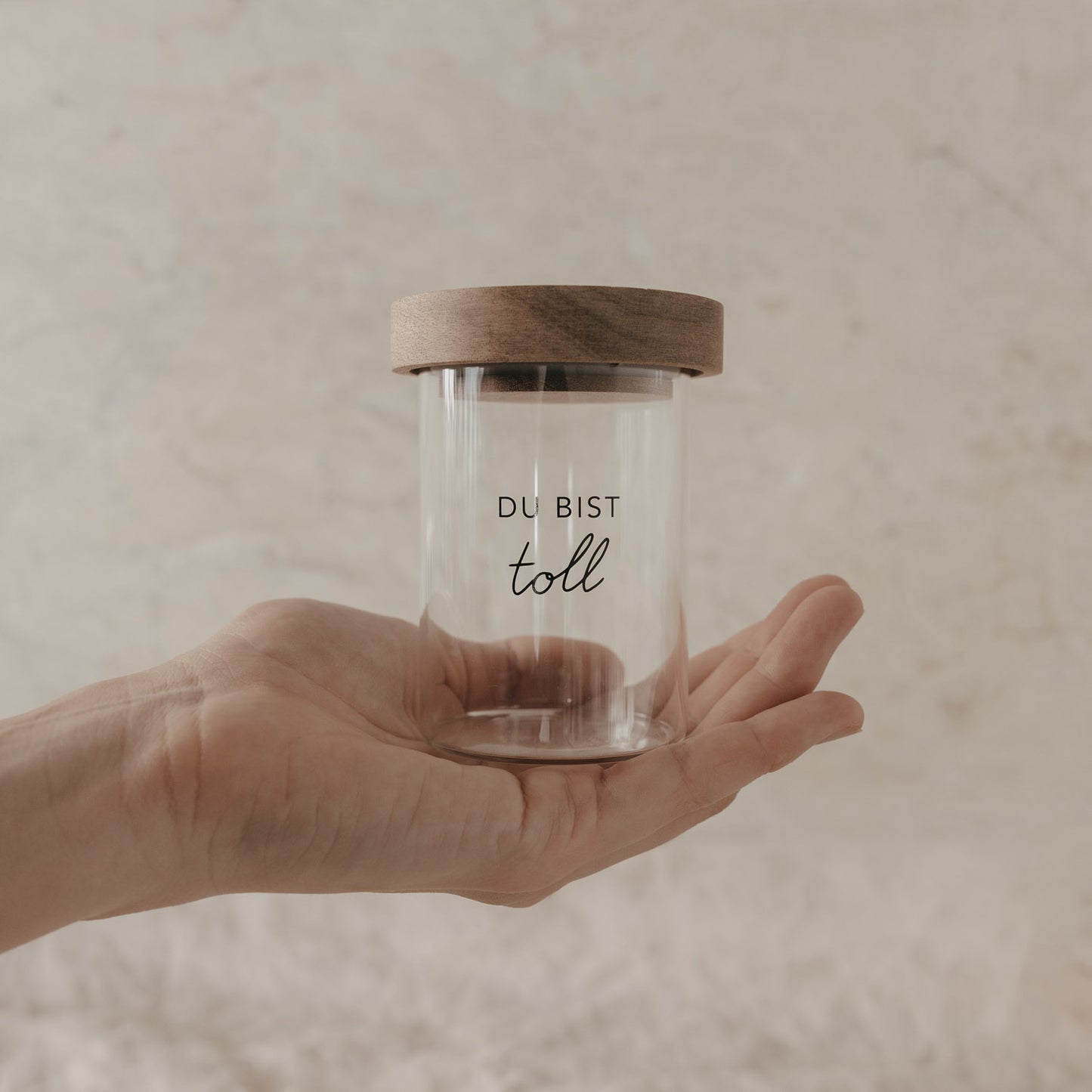 Kleines Vorratsglas mit Holzdeckel und Schriftzug „Du bist toll“ in einer Hand