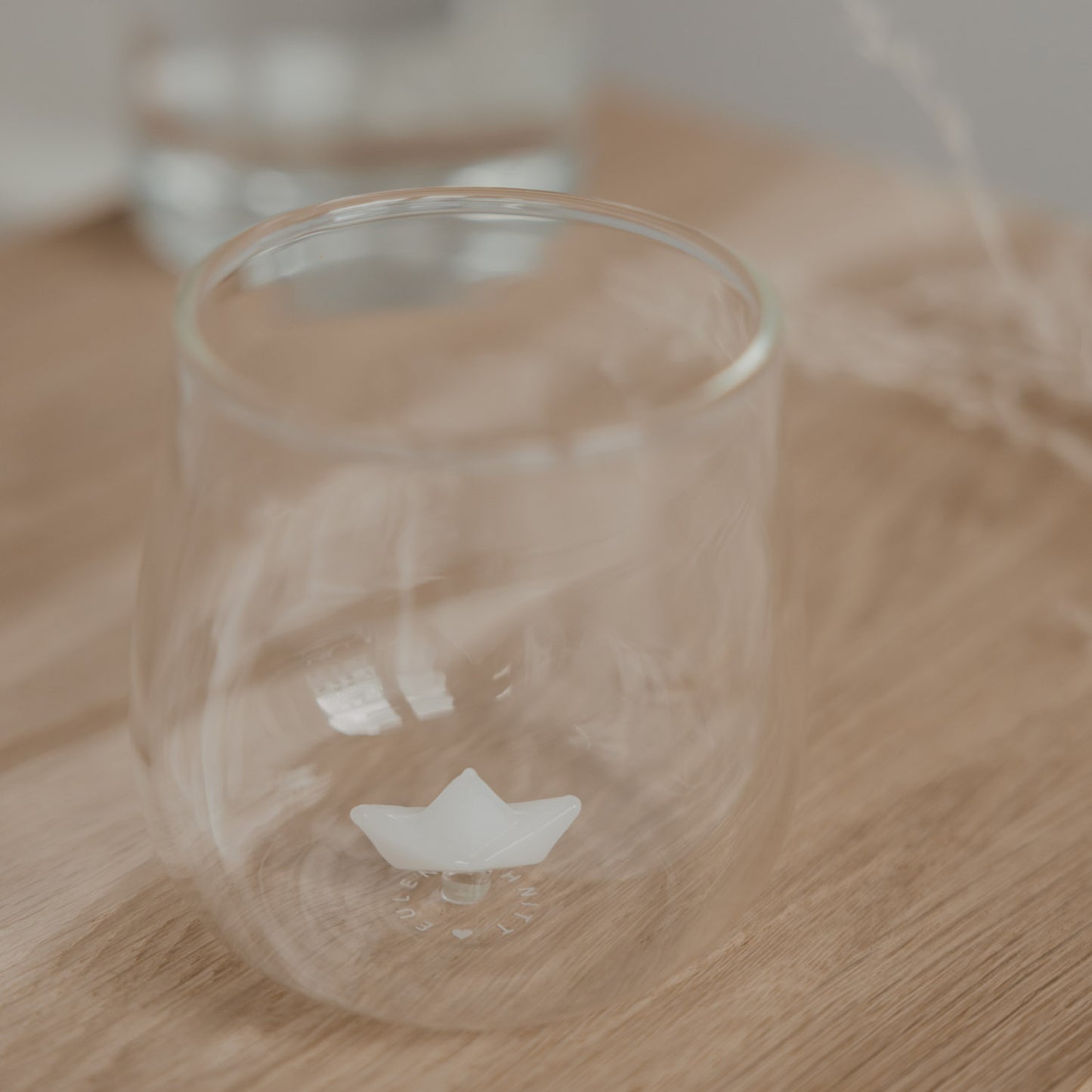 Minimalistisches Trinkglas mit Papierboot Design auf Holzbrett, stilvolles Glas für Getränke