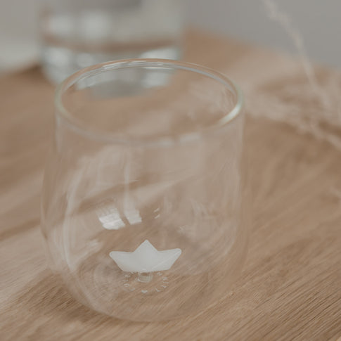 Minimalistisches Trinkglas mit Papierboot Design auf Holzbrett, stilvolles Glas für Getränke