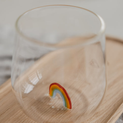 Detailaufnahme Glas mit buntem Regenbogen am Boden, modernes Trinkglas auf Holztablett