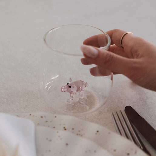 Hand hält doppelwandiges Glas mit rosa Schwein-Motiv, stilvolles Trinkglas im Alltagseinsatz