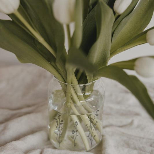 Detailaufnahme einer Glasvase mit filigranem Blumenwiesen-Print und Tulpenstielen im Wasser