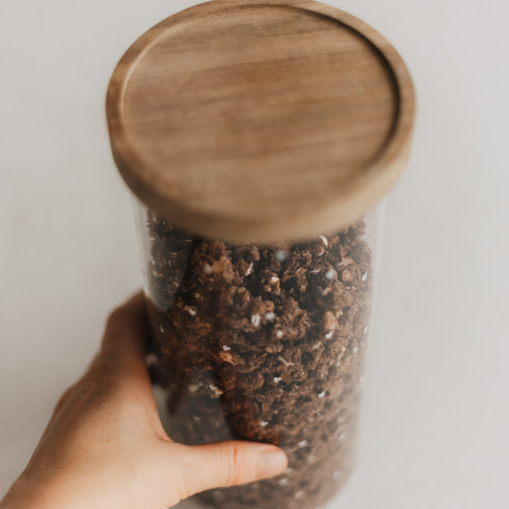 Hand hält eine Glasdose mit weißen Herzen, Schoko-Müsli und rundem Holzdeckel