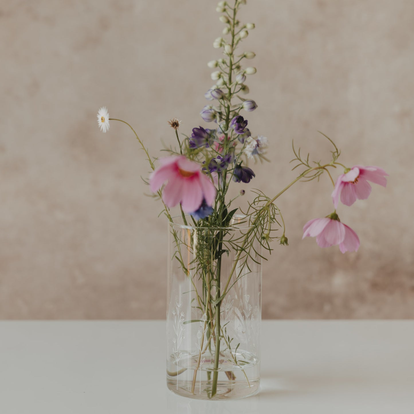 Hoher Glasbehälter mit weißem Wildblumen-Motiv und Holzdeckel, als Vase mit bunten Wiesenblumen dekoriert