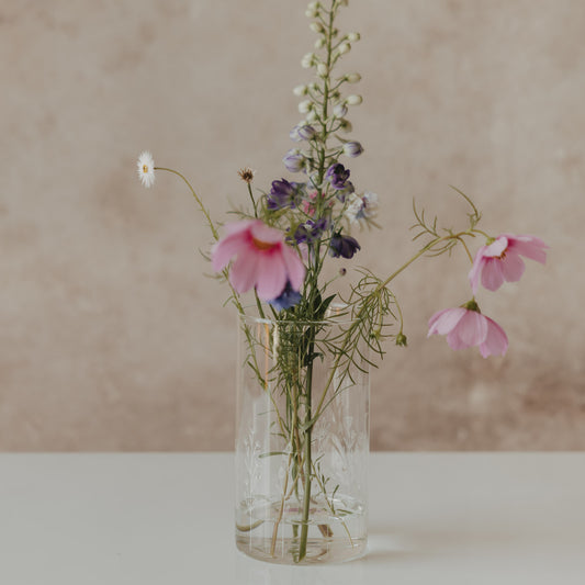 Hoher Glasbehälter mit weißem Wildblumen-Motiv und Holzdeckel, als Vase mit bunten Wiesenblumen dekoriert