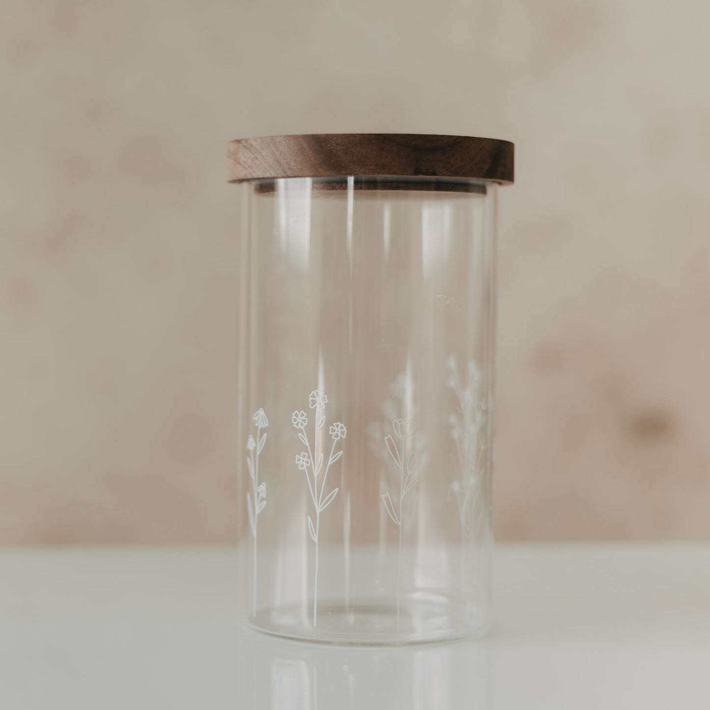 Leerer hoher Glas-Vorratsbehälter mit filigranem weißem Wildblumen-Motiv und dunklem Holzdeckel