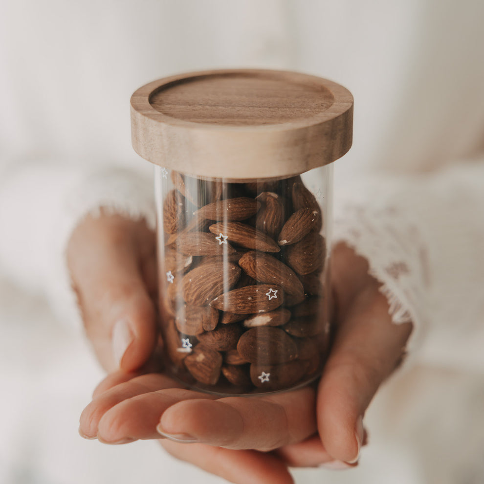 Mini Vorratsglas mit Sternen und Holzdeckel, gefüllt mit Mandeln und in den Händen gehalten