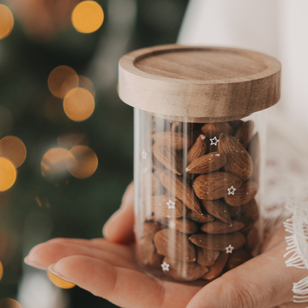 Mini Vorratsglas mit Sternen und Holzdeckel, gefüllt mit Mandeln vor weihnachtlicher Kulisse