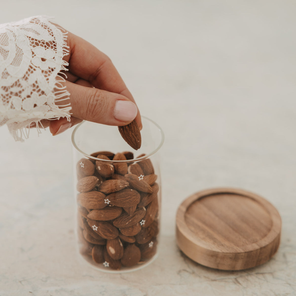 Offenes Mini Vorratsglas mit Sternen und Mandeln, daneben der abgenommene Holzdeckel