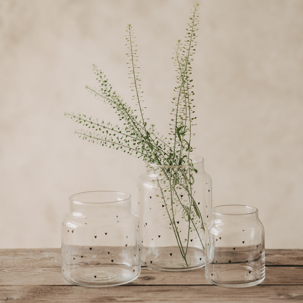 Glasvasen mit Herzprint als Set dekoriert mit grünen Zweigen auf Holztisch
