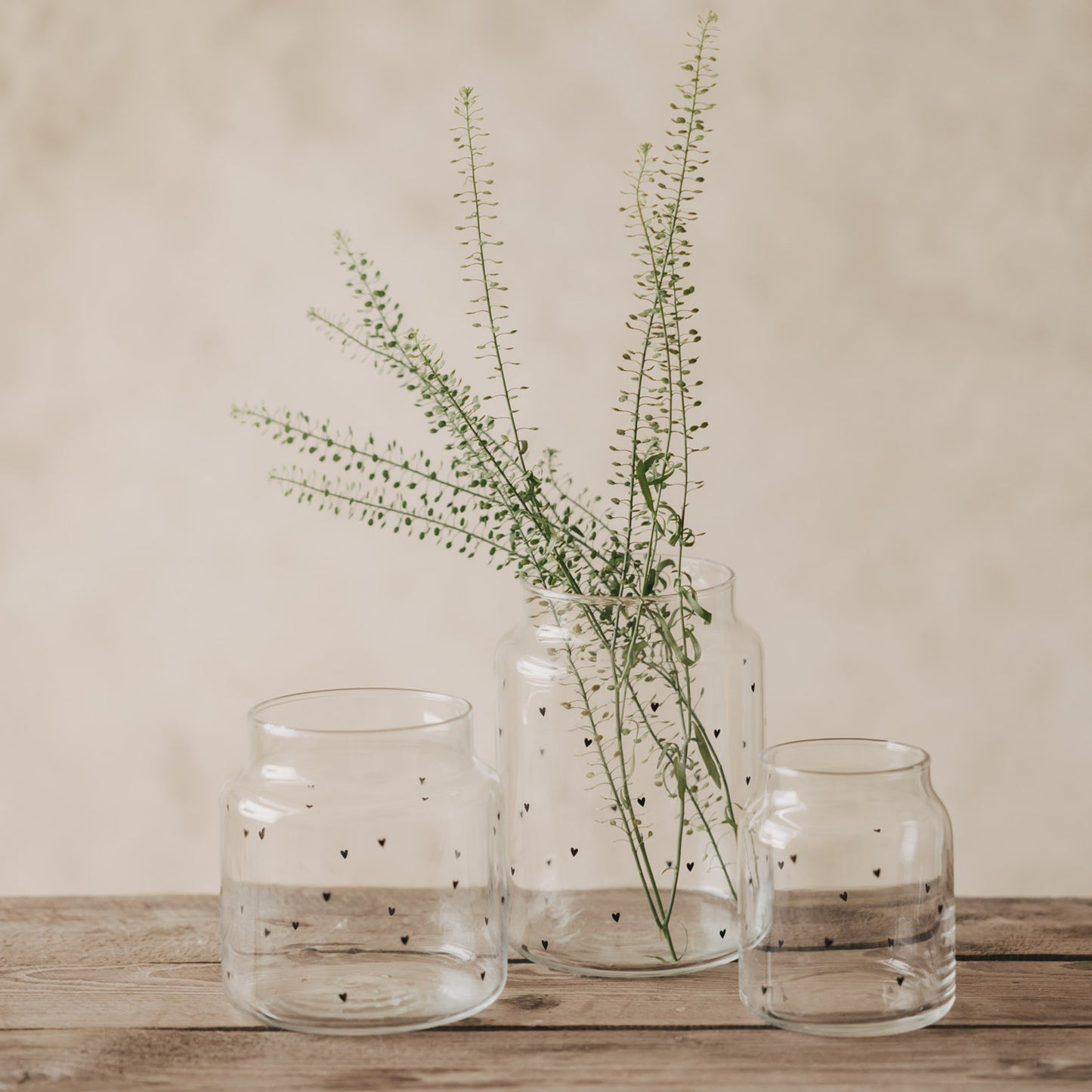 Glasvasen mit Herzprint als Set dekoriert mit grünen Zweigen auf Holztisch