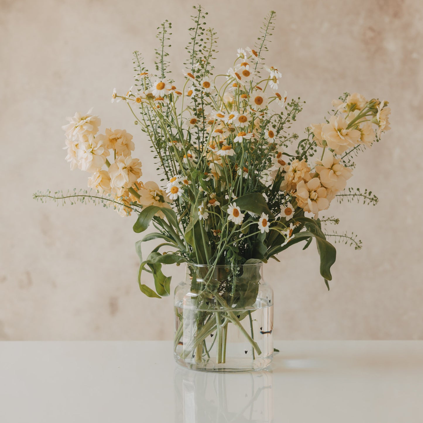Glasvase mit schwarzen Herzen und vollem Blumenarrangement
