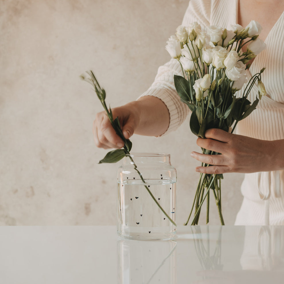 Glasvase mit schwarzen Herzen wird mit weißen Blumen bestückt