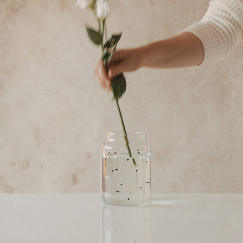 Glasvase mit schwarzen Herzen beim Arrangieren von Blumen