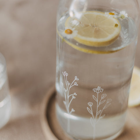 Detail einer Glas Karaffe mit Zitronenscheibe und kleinen Blüten im Wasser
