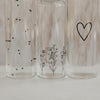 Glas Trinkflaschen mit Herz und Blumenwiese Design in Nahaufnahme, minimalistisch