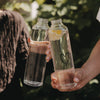 Zwei Trinkflaschen aus Glas mit Herzmotiv und Zitronenwasser in der Hand