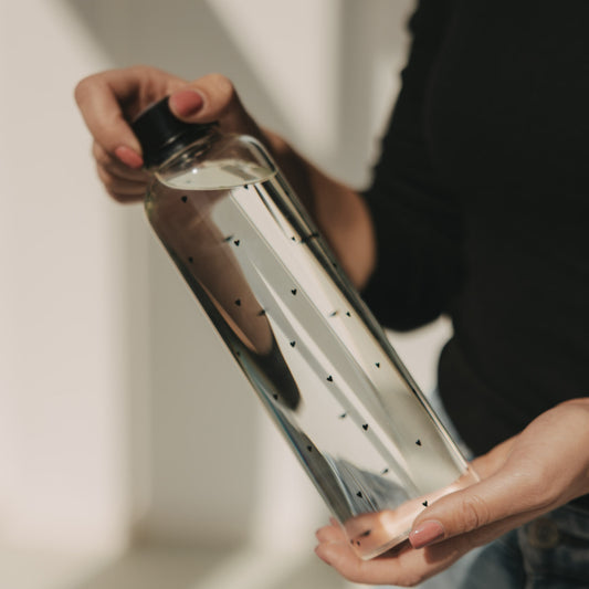 Trinkflasche aus Glas mit Herzmuster, schräg gehalten, modernes Design, Nahaufnahme in der Hand