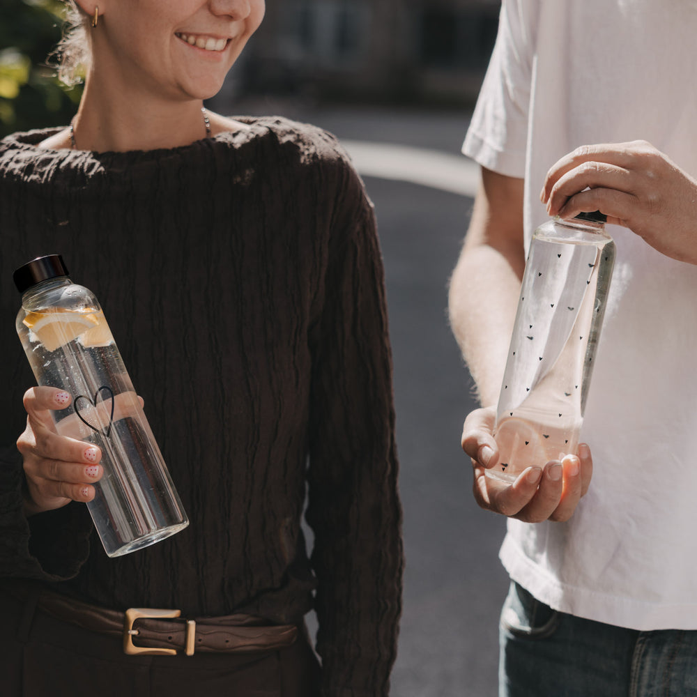 Zwei Personen halten Glas Trinkflaschen mit Herzmotiv, gefüllt mit Wasser und Zitrone, unterwegs