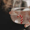 Nahaufnahme des Trinkglases mit Wasser und rot-weißer Zuckerstange als dekorative Figur im Glasboden.