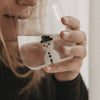 Nahaufnahme einer Frau beim Trinken aus einem transparenten Figurenglas mit Schneemann und schwarzem Hut.
