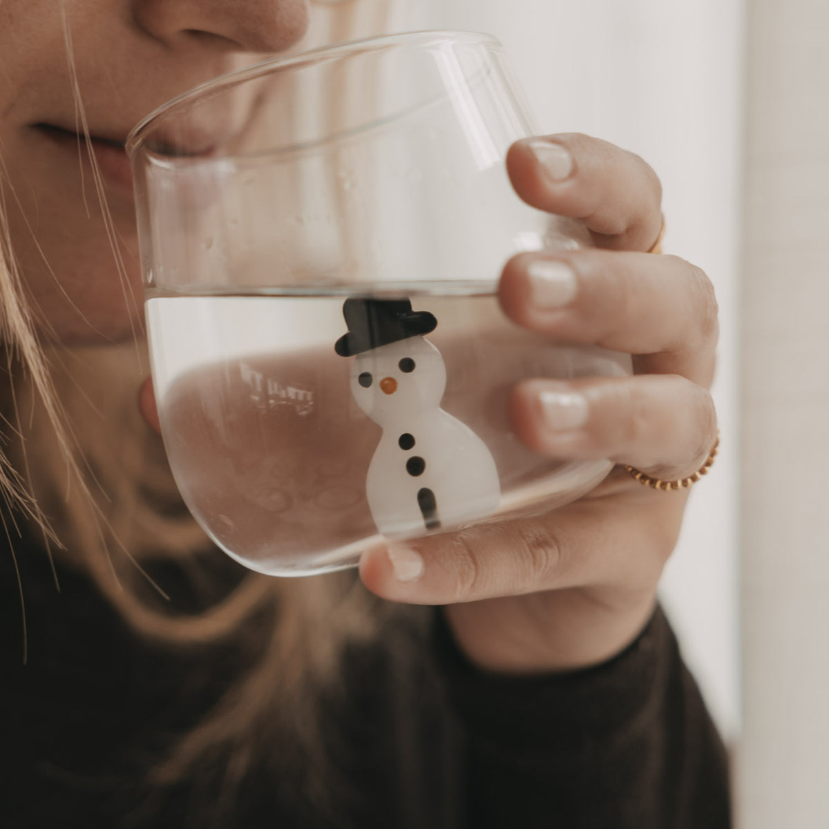 Nahaufnahme einer Frau beim Trinken aus einem transparenten Figurenglas mit Schneemann und schwarzem Hut.